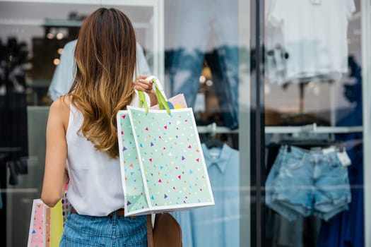 A happy customer carrying shopping bags stands in front of a store window, admiring the fashion display. She's excited about the sale and ready to spend on her favorite styles.