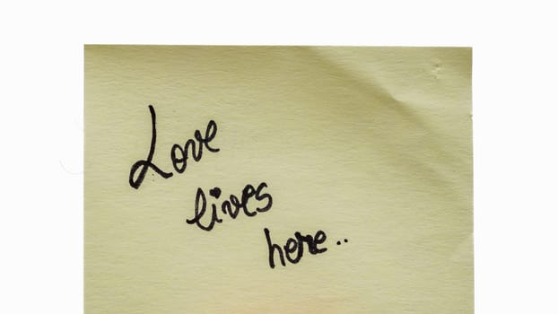 Love lives here handwriting text close up isolated on yellow paper with copy space.