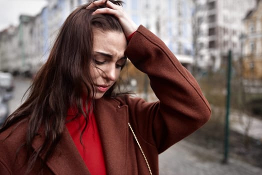 Portrait of frustrated young woman on the street in a warm coat touching her head in mental paint. depression concept