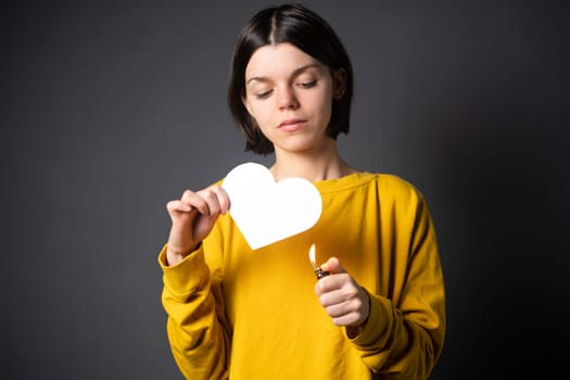 The woman sets the heart on fire, the end of the romantic relationship. Young girl sets fire to a white paper heart, declaring war on inequality in the toxic abusive relationship in which she was.