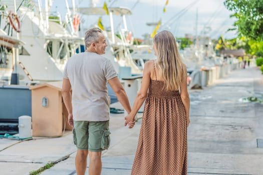 A happy, mature couple over 40, enjoying a leisurely walk on the waterfront, their joy evident as they embrace the journey of pregnancy later in life.