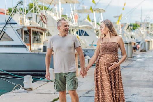 A happy, mature couple over 40, enjoying a leisurely walk on the waterfront, their joy evident as they embrace the journey of pregnancy later in life.