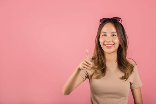 Portrait Asian beautiful young woman smiling she standing made finger thumbs up, Ok sign to agree studio shot isolated on pink background, Thai female successful like finger gesture with copy space