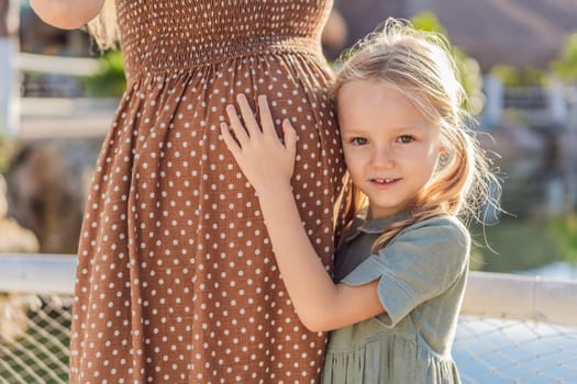 A heartwarming moment captured as a daughter lovingly embraces her mother's pregnant belly, sharing in the excitement and anticipation of a new family member.