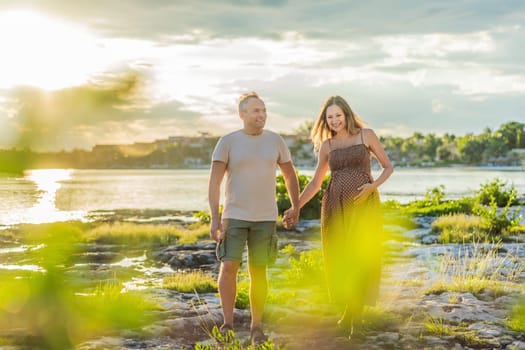 A happy, mature couple over 40, enjoying a leisurely walk on the waterfront On the Sunset, their joy evident as they embrace the journey of pregnancy later in life.