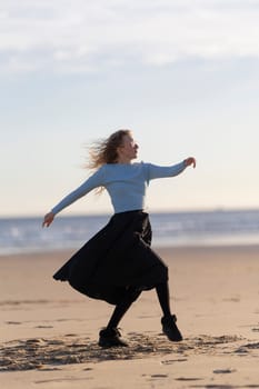 A woman is standing on the beach, wearing a blue shirt and black skirt. She is dancing and she is enjoying herself. The beach setting and the woman's carefree attitude create a sense of relaxation