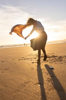 A woman is dancing on the beach in the evening. The sun is setting in the background, casting a warm glow on the scene. The woman's movements are graceful and fluid, as if she is in a dance