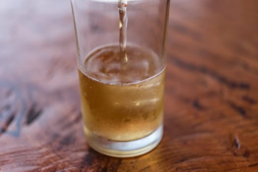 Pouring brewing cold beer water in to beer glass with ice and froth in brewery pub or restaurant on a wood table