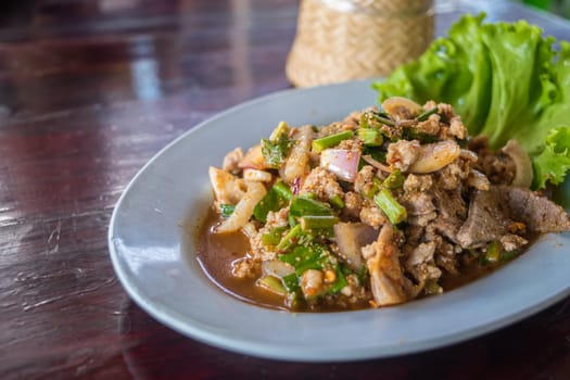 Spicy minced pork salad or Ground pork salad (Laab) is a Thai food for health consists of pork, ground rice, chili, lemon, onion and herb mixed in plate on a wood table at Thai street food