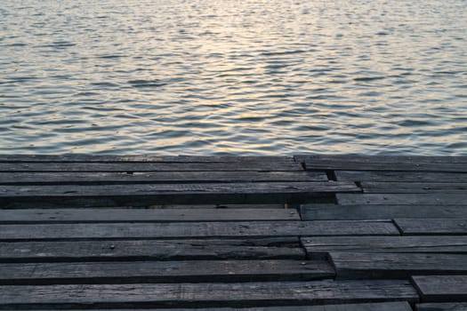 Sunlight in sunset time reflection on water wave in lake with wood floor