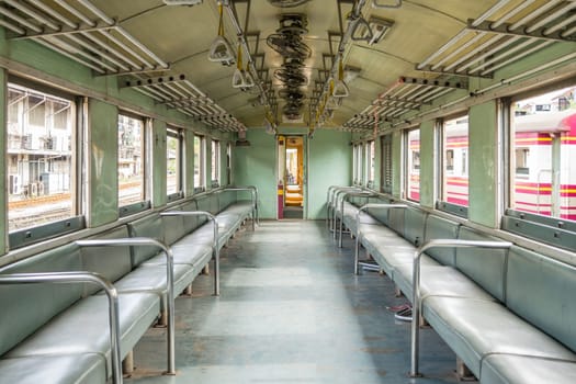 Inside of old public Thai railway train cabin with seats, handrails, fan and interior in vintage style service for passenger transport