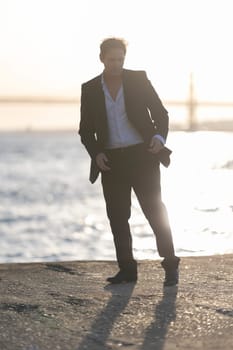 Businessman is striking a pose by the water at sunset