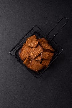 Crispy homemade brown bread chips with seeds and grains, salt, spices and herbs on a dark concrete background