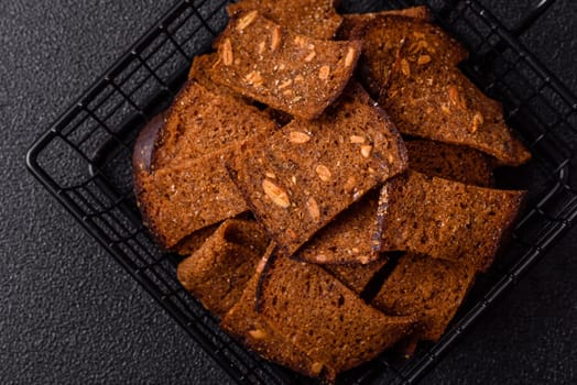 Crispy homemade brown bread chips with seeds and grains, salt, spices and herbs on a dark concrete background
