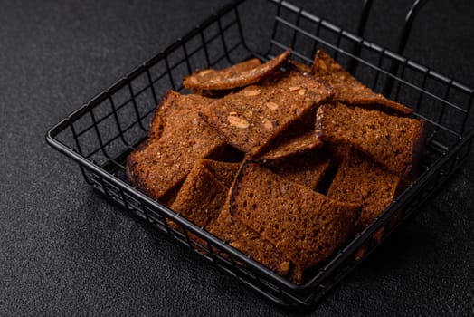 Crispy homemade brown bread chips with seeds and grains, salt, spices and herbs on a dark concrete background