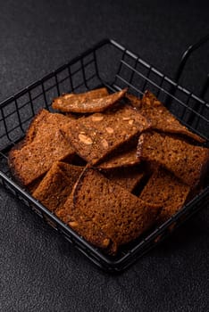 Crispy homemade brown bread chips with seeds and grains, salt, spices and herbs on a dark concrete background