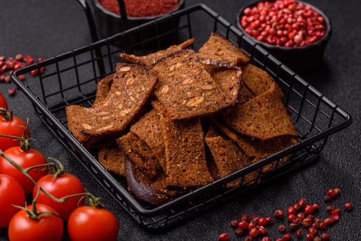 Crispy homemade brown bread chips with seeds and grains, salt, spices and herbs on a dark concrete background