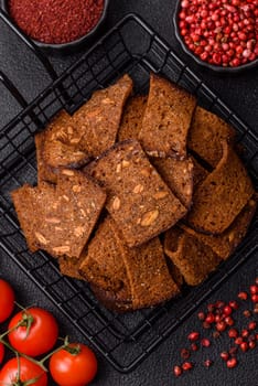 Crispy homemade brown bread chips with seeds and grains, salt, spices and herbs on a dark concrete background