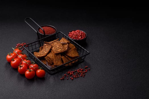 Crispy homemade brown bread chips with seeds and grains, salt, spices and herbs on a dark concrete background