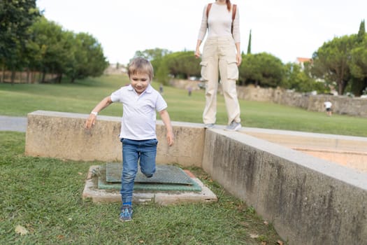 A young boy runs across a grassy field with a woman watching him. The scene is peaceful and joyful, with the boy enjoying his time outdoors