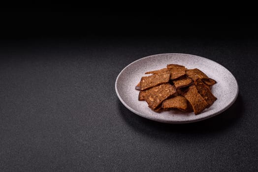 Crispy homemade brown bread chips with seeds and grains, salt, spices and herbs on a dark concrete background
