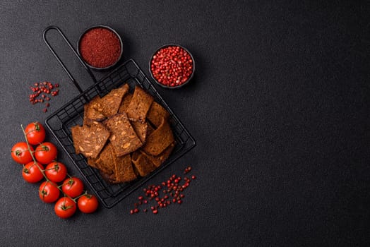 Crispy homemade brown bread chips with seeds and grains, salt, spices and herbs on a dark concrete background