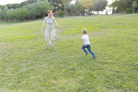 Mother and son are running through a grassy park on a sunny day