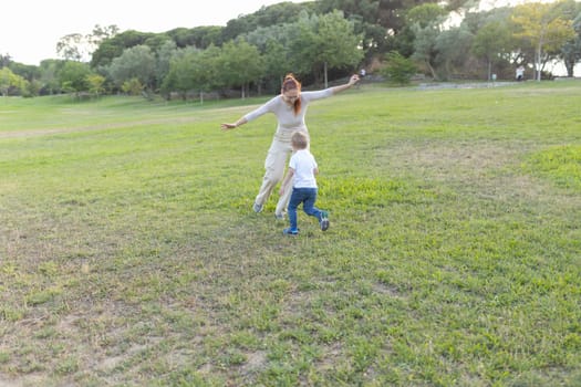 Mother and her son are enjoying a beautiful day outdoors, playing tag in a grassy park