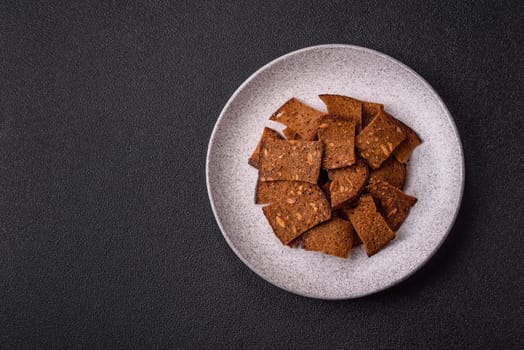 Crispy homemade brown bread chips with seeds and grains, salt, spices and herbs on a dark concrete background