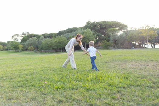 Mother and her son are happily playing in a grassy park on a sunny day