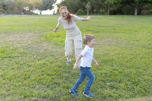 Mother and her son are running through a grassy park on a sunny day