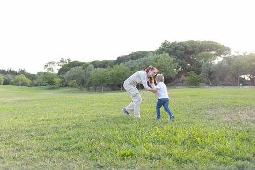 Mother and son having fun together while running on the grass in the park