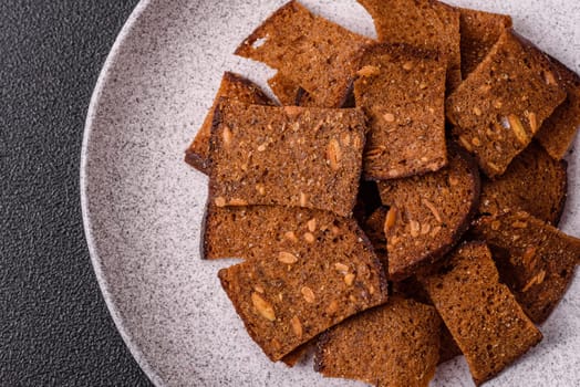Crispy homemade brown bread chips with seeds and grains, salt, spices and herbs on a dark concrete background