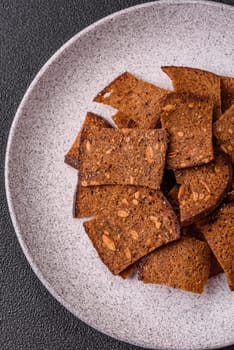 Crispy homemade brown bread chips with seeds and grains, salt, spices and herbs on a dark concrete background