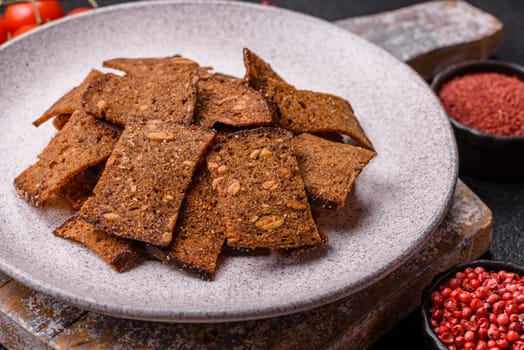 Crispy homemade brown bread chips with seeds and grains, salt, spices and herbs on a dark concrete background