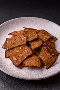 Crispy homemade brown bread chips with seeds and grains, salt, spices and herbs on a dark concrete background
