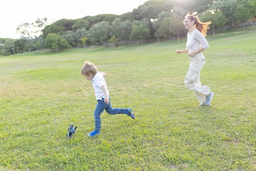 Mother and her son are running and playing together in a grassy park