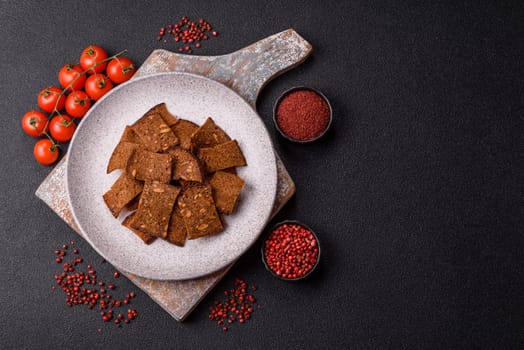 Crispy homemade brown bread chips with seeds and grains, salt, spices and herbs on a dark concrete background