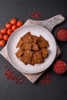 Crispy homemade brown bread chips with seeds and grains, salt, spices and herbs on a dark concrete background