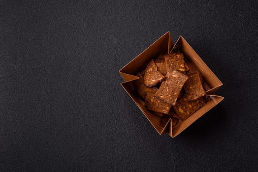 Crispy homemade brown bread chips with seeds and grains, salt, spices and herbs on a dark concrete background