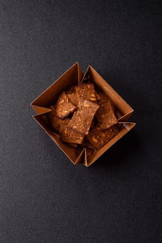 Crispy homemade brown bread chips with seeds and grains, salt, spices and herbs on a dark concrete background