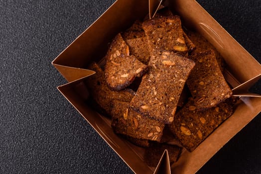 Crispy homemade brown bread chips with seeds and grains, salt, spices and herbs on a dark concrete background