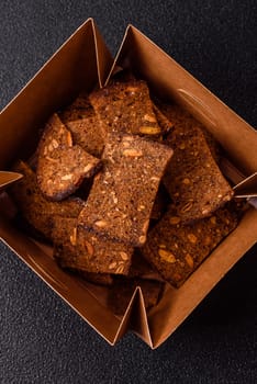 Crispy homemade brown bread chips with seeds and grains, salt, spices and herbs on a dark concrete background