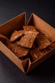 Crispy homemade brown bread chips with seeds and grains, salt, spices and herbs on a dark concrete background