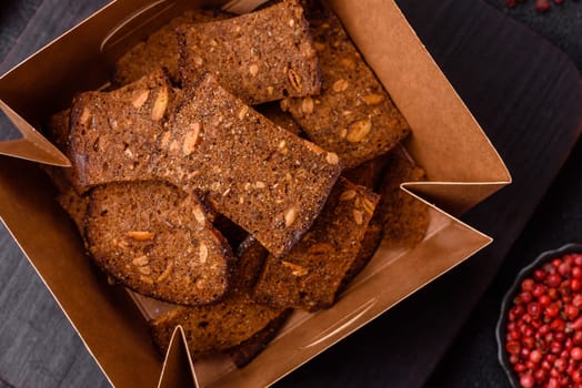 Crispy homemade brown bread chips with seeds and grains, salt, spices and herbs on a dark concrete background