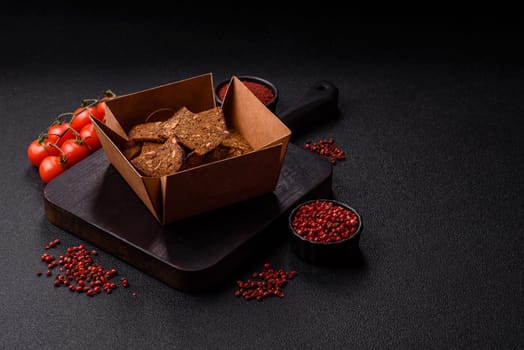 Crispy homemade brown bread chips with seeds and grains, salt, spices and herbs on a dark concrete background