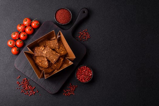 Crispy homemade brown bread chips with seeds and grains, salt, spices and herbs on a dark concrete background