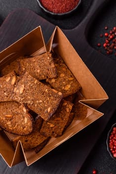 Crispy homemade brown bread chips with seeds and grains, salt, spices and herbs on a dark concrete background