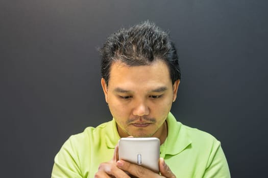 Asian man 40s have a short hair in polo shirt smiling have a thinking gesture with doubt and thoughtful concept using smartphone on black background dark style