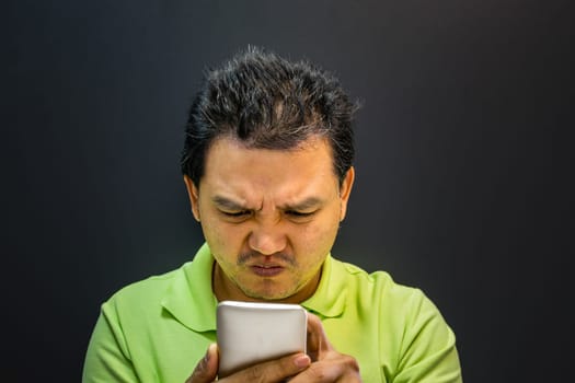 Asian man 40s have a short hair in polo shirt strain have a unhappy gesture with failure and problems concept using smartphone on black background dark style